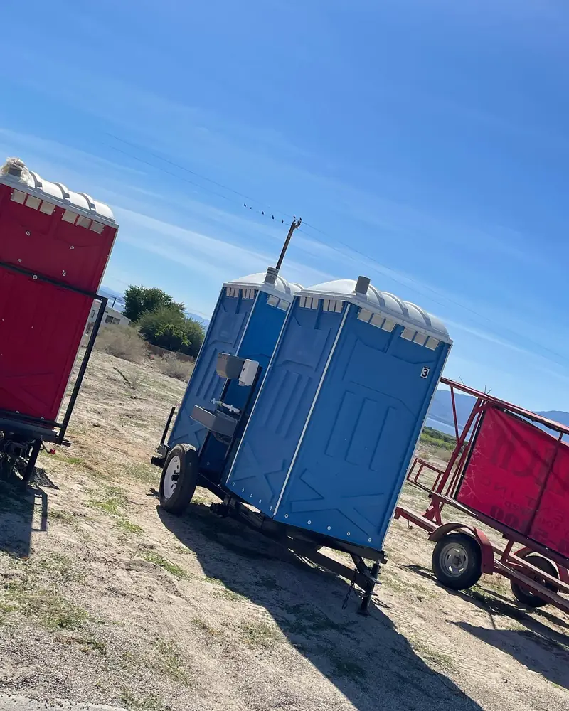 Blue portable toilets loaded on a delivery trailer at a dirt construction site