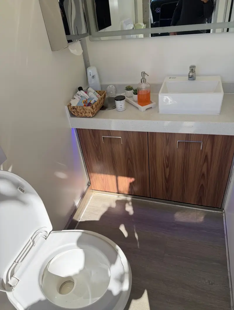 Wood vanity and flush toilet in a restroom trailer stall.