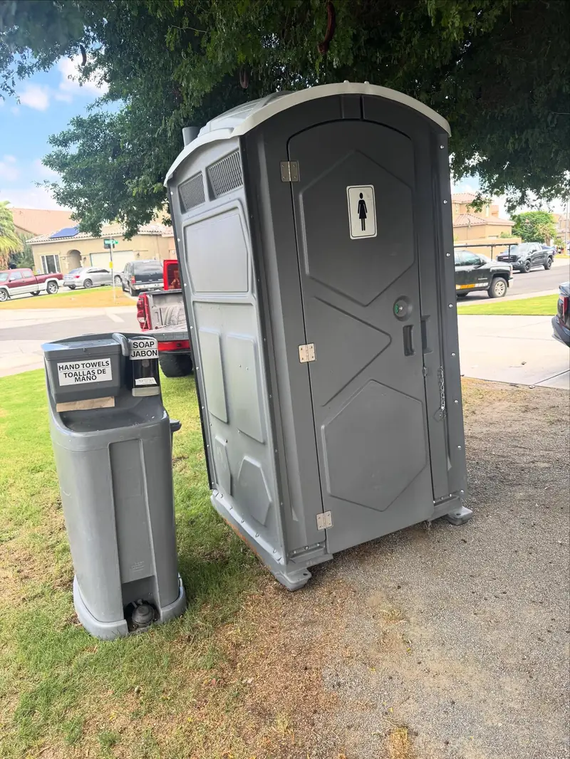 Gray portable toilet with a standalone hand-washing station on grass